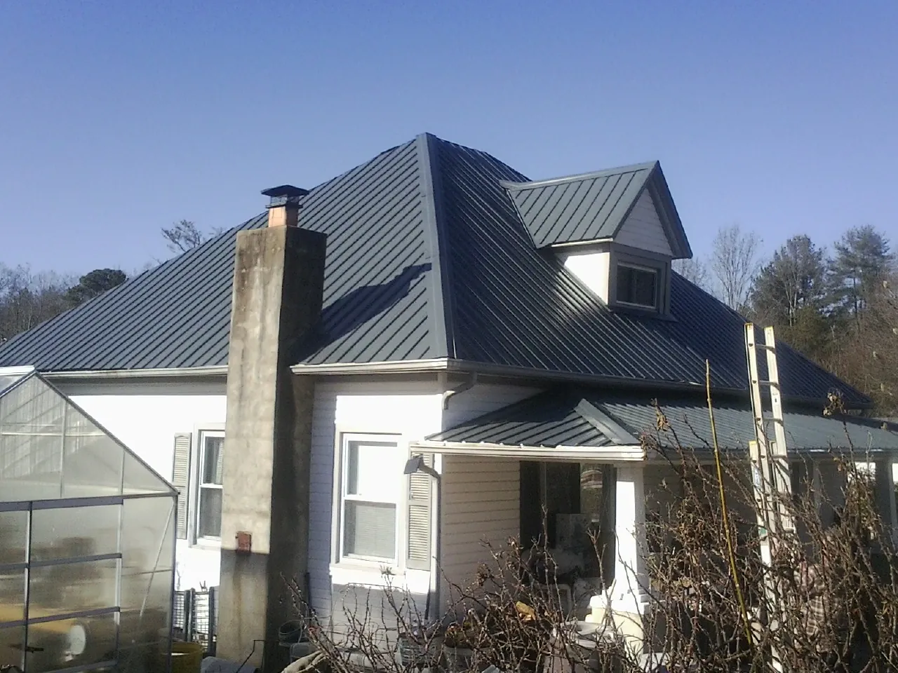 Dark blue standing seam metal roof on a white farmhouse with dormer in Freedom
