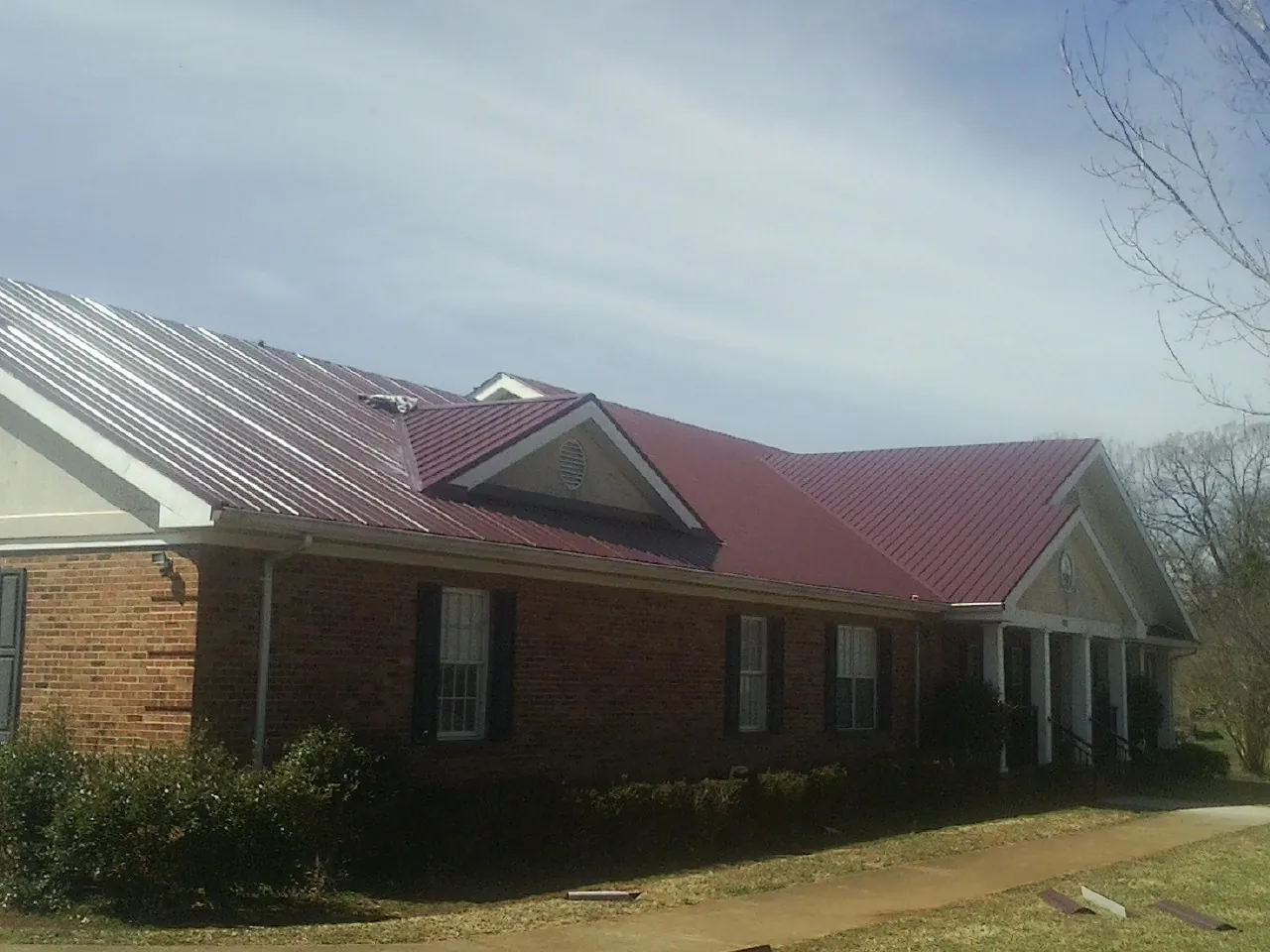 Red metal roof with gabled entries on a long brick building, from a Hail Damage Roof Repair job in Freedom